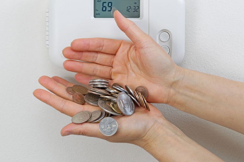 Homeowner holding a lot of change in front of thermostat to represent how to save money on your AC bill.